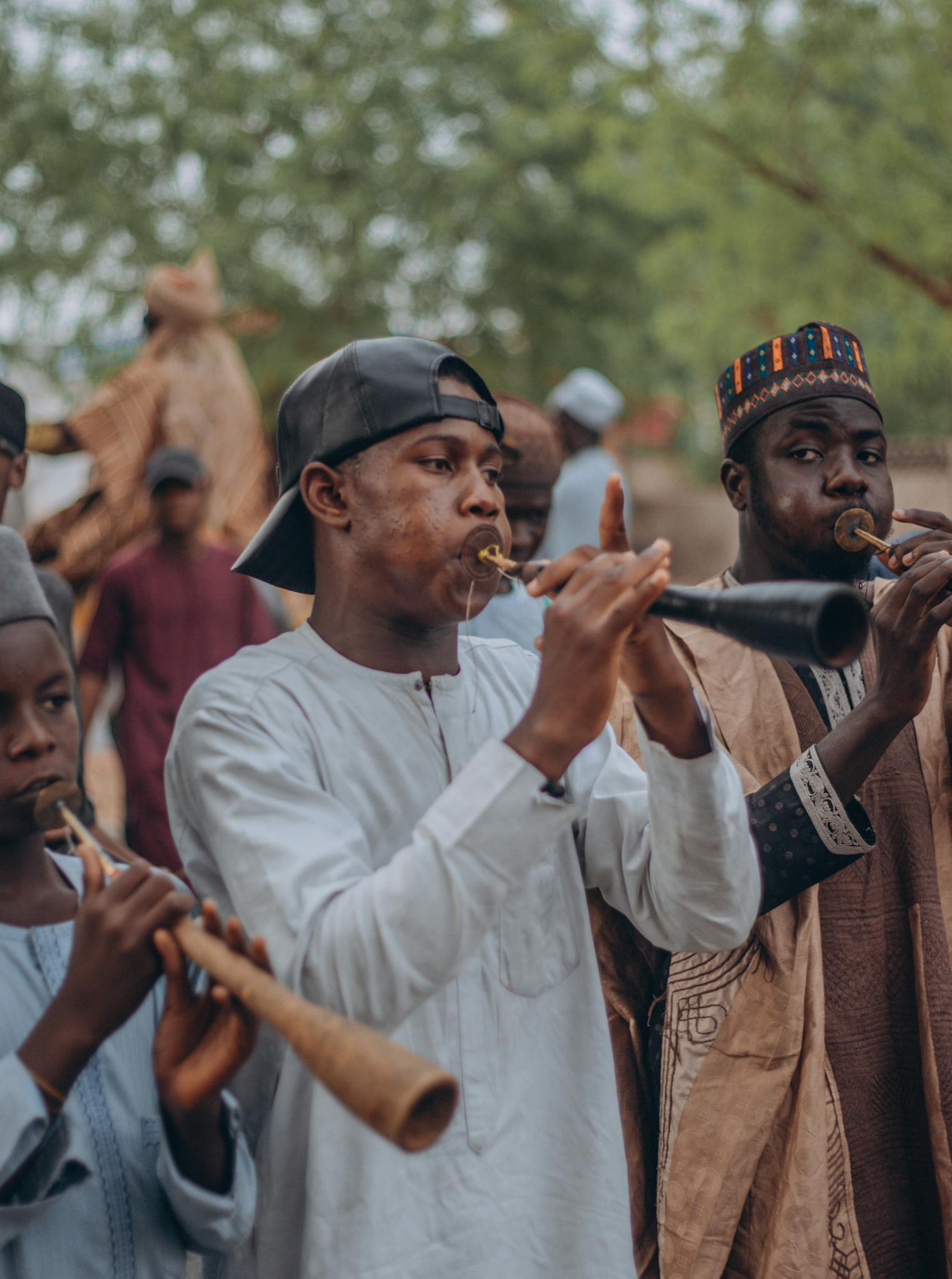 Group of African men wearing traditional attire playing wind instruments in a cultural setting.