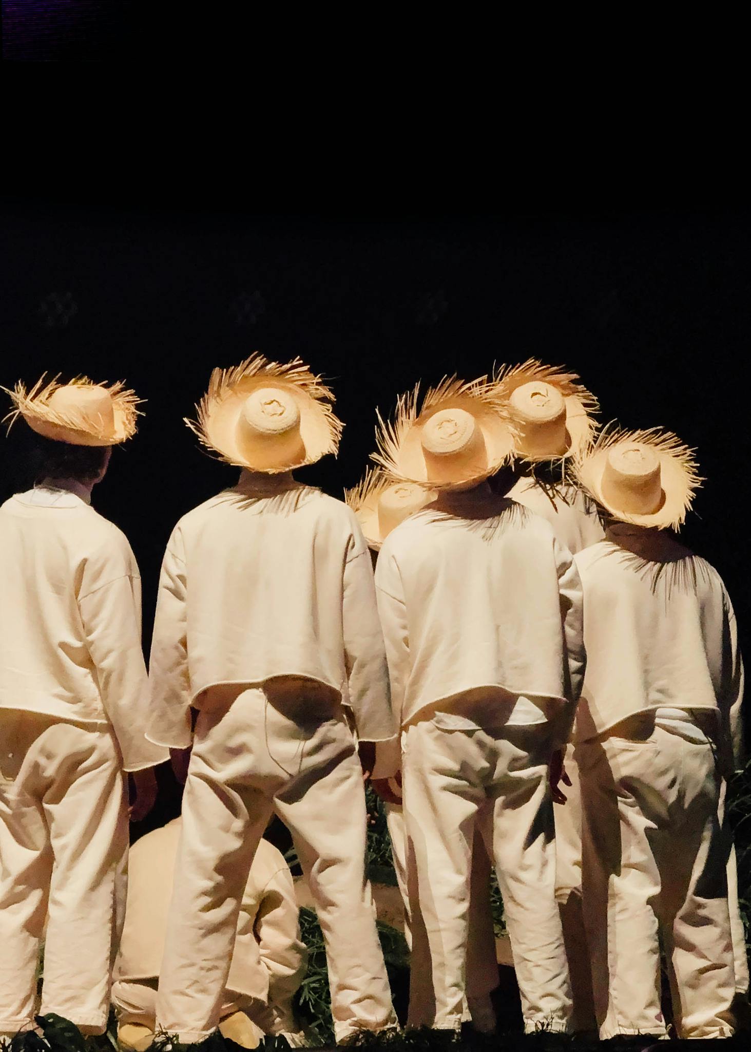 Rear view of dancers in straw hats performing traditional dance on stage.